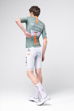 Male cyclist wearing Gobik Netcompany INEOS Grenadier green jersey and white bib shorts, rear view