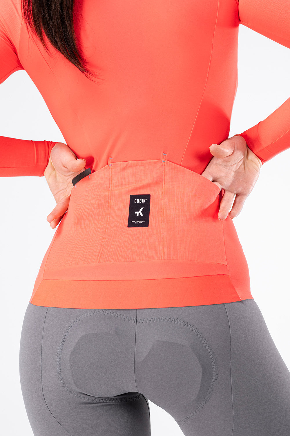 Female model showing rear pockets of Gobik Avalon long sleeve jersey in lava colorway
