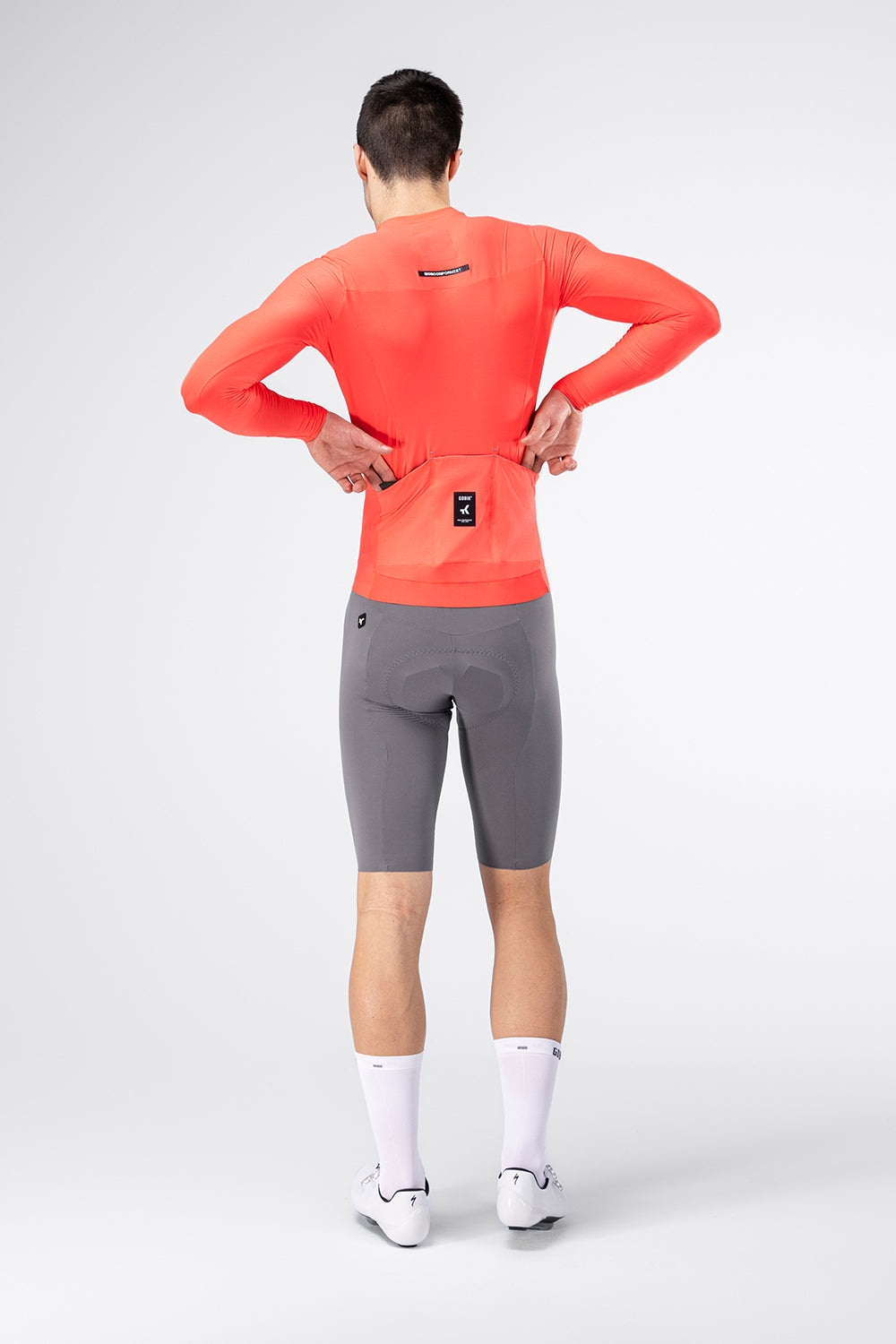 Male model wearing Gobik Avalon long sleeve jersey in lava from behind with gray cycling shorts