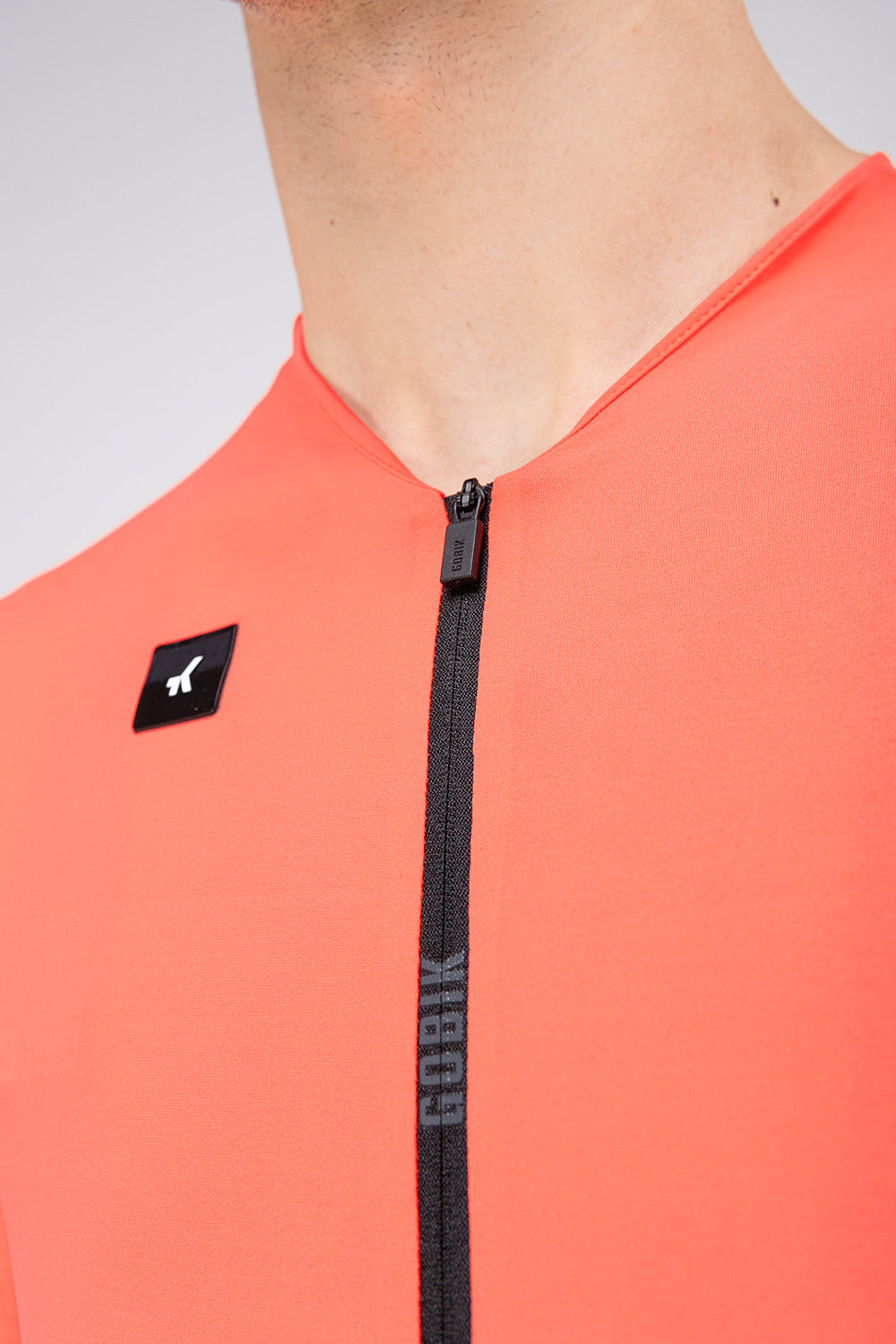 Close-up of Gobik Avalon Jersey zipper and brand logo patch in Lava coral color