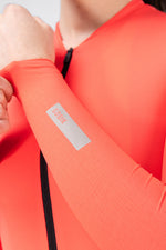 Close-up of Gobik Avalon Jersey sleeve reflective logo badge on female model in Lava color