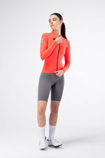 Gobik Avalon Long Sleeve Jersey in Lava color, female model front view with gray cycling shorts