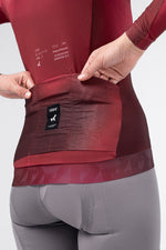 Detail of Gobik Vanquish jersey rear pockets with brand label in Monarch burgundy on female model
