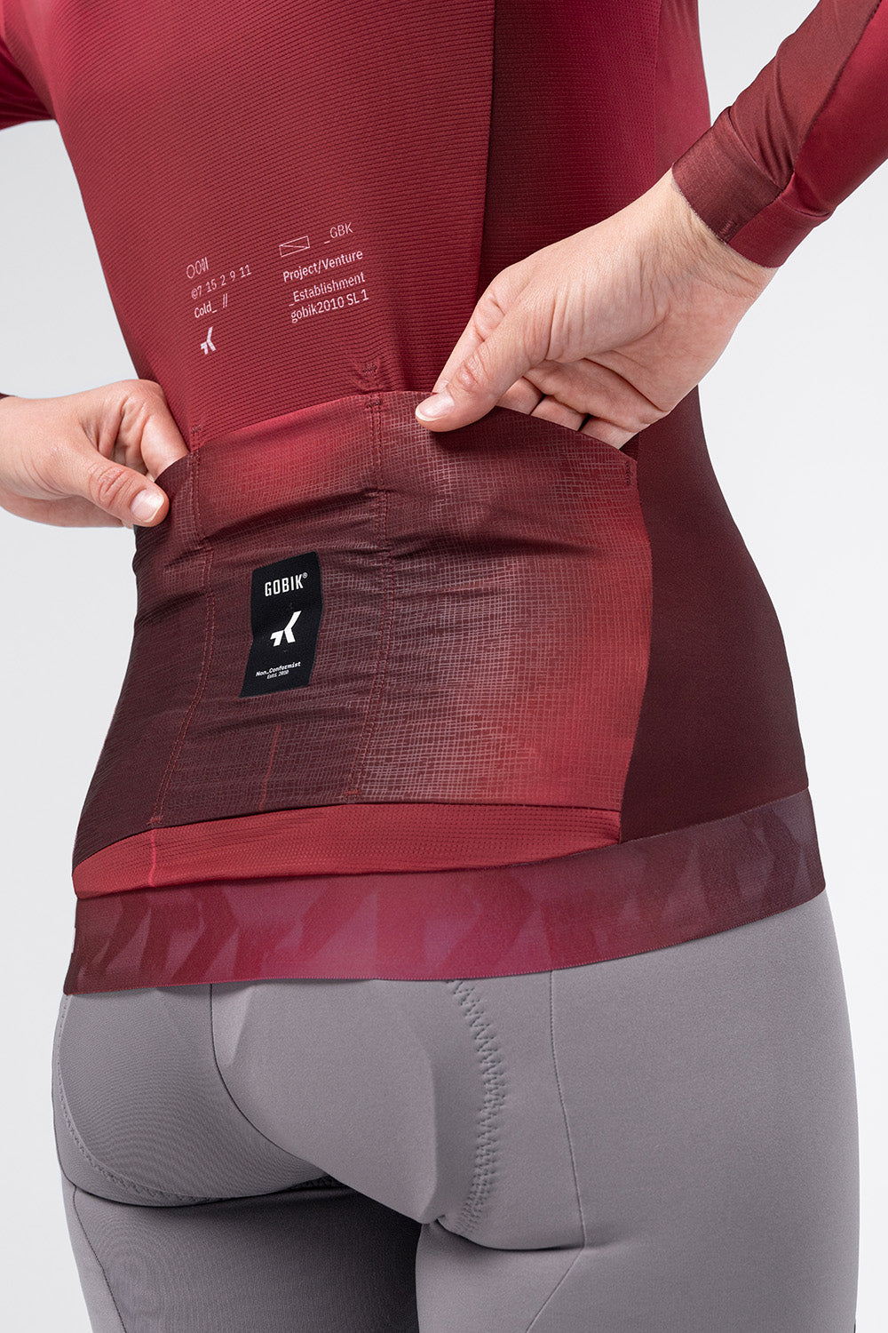 Detail of Gobik Vanquish jersey rear pockets with brand label in Monarch burgundy on female model