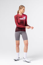 Female model side view wearing Gobik Vanquish long sleeve jersey in Monarch red with grey cycling shorts
