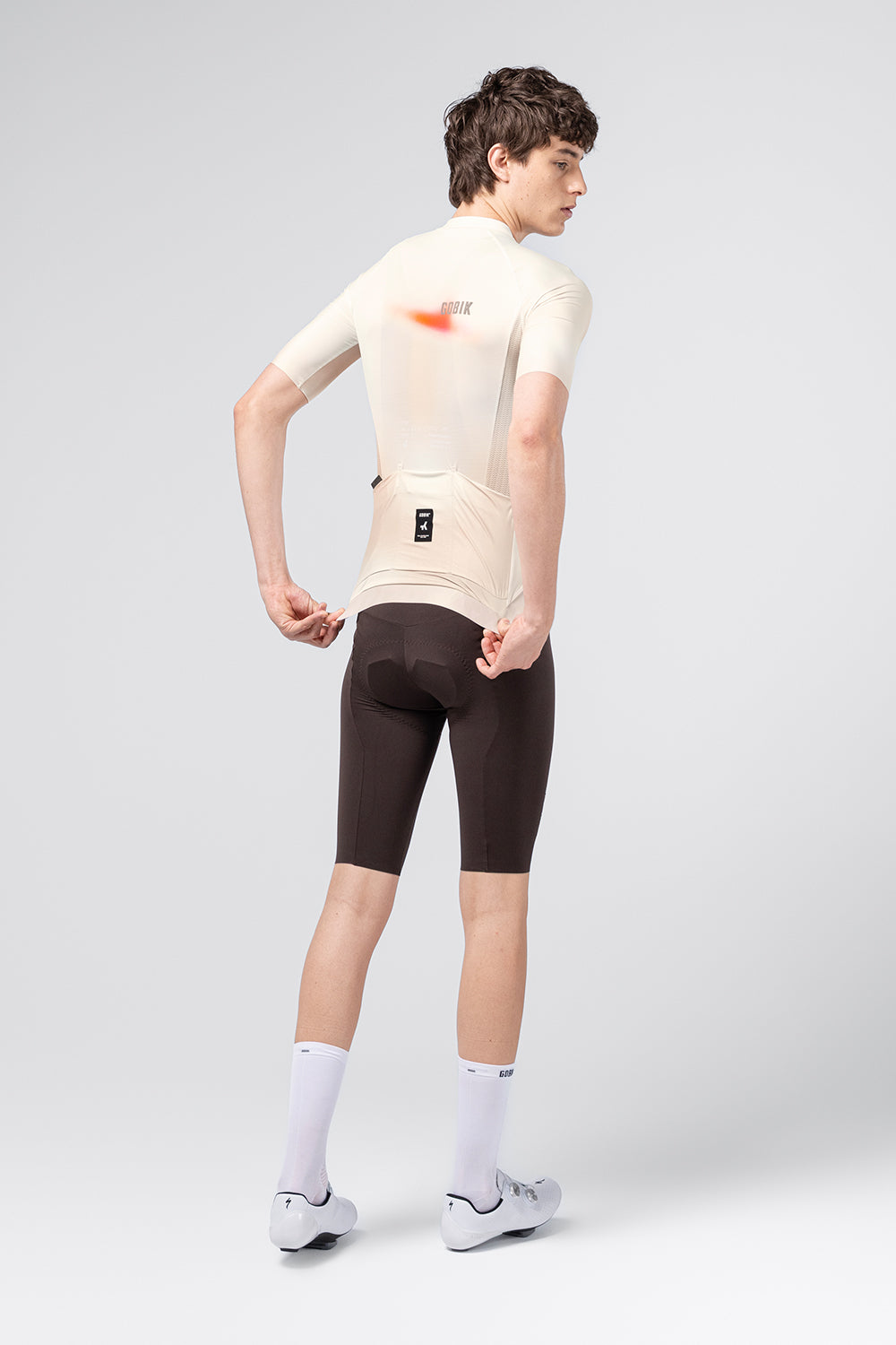 Male model wearing Gobik CX Pro 4.0 almond cycling jersey with dark brown shorts, rear view