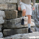 Person wearing Thorlos grey crew socks with black shoes climbing rocky stone steps near waterfall