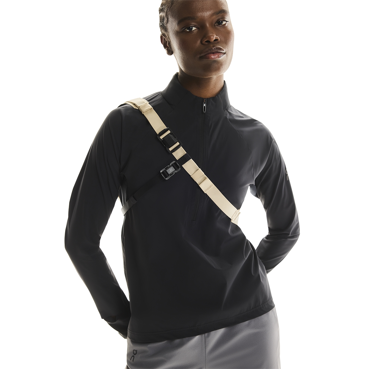 Model wearing On Sling Pack 9L in Biscuit and Black colorway over black athletic jacket