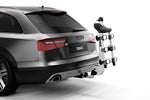 Thule hitch-mounted bike rack attached to rear of silver Audi wagon on white background