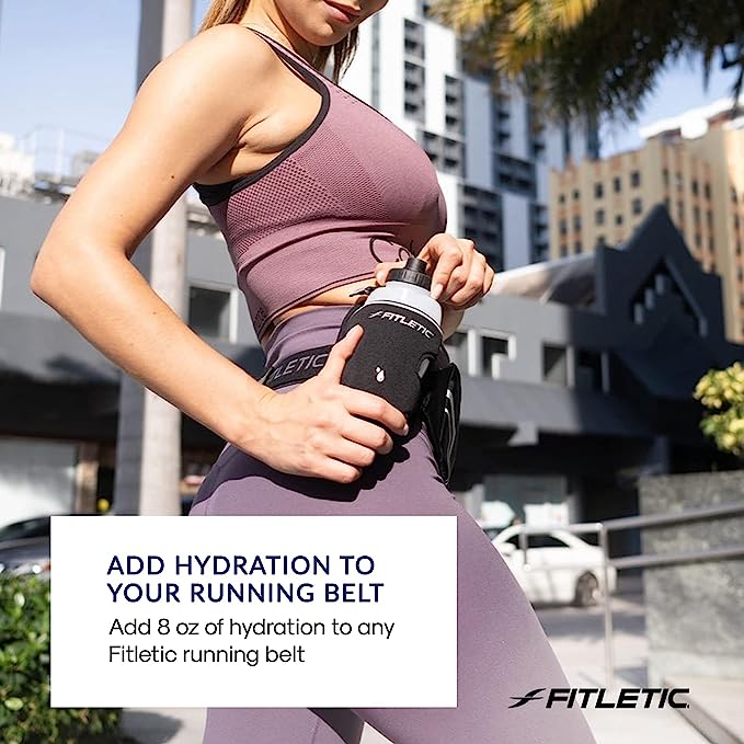 Female runner accessing Fitletic black water bottle holster on running belt outdoors in urban setting
