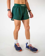 Model wearing ChicknLegs forest green 4-inch half split running shorts with elastic waistband