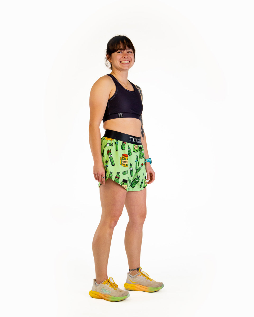 Woman wearing green pickle-patterned running shorts with navy sports bra on white background