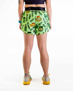 Woman wearing green pickle-patterned split running shorts, back view on white background