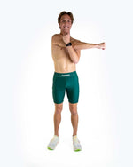 Athletic man wearing forest green ChicknLegs compression shorts against white studio background