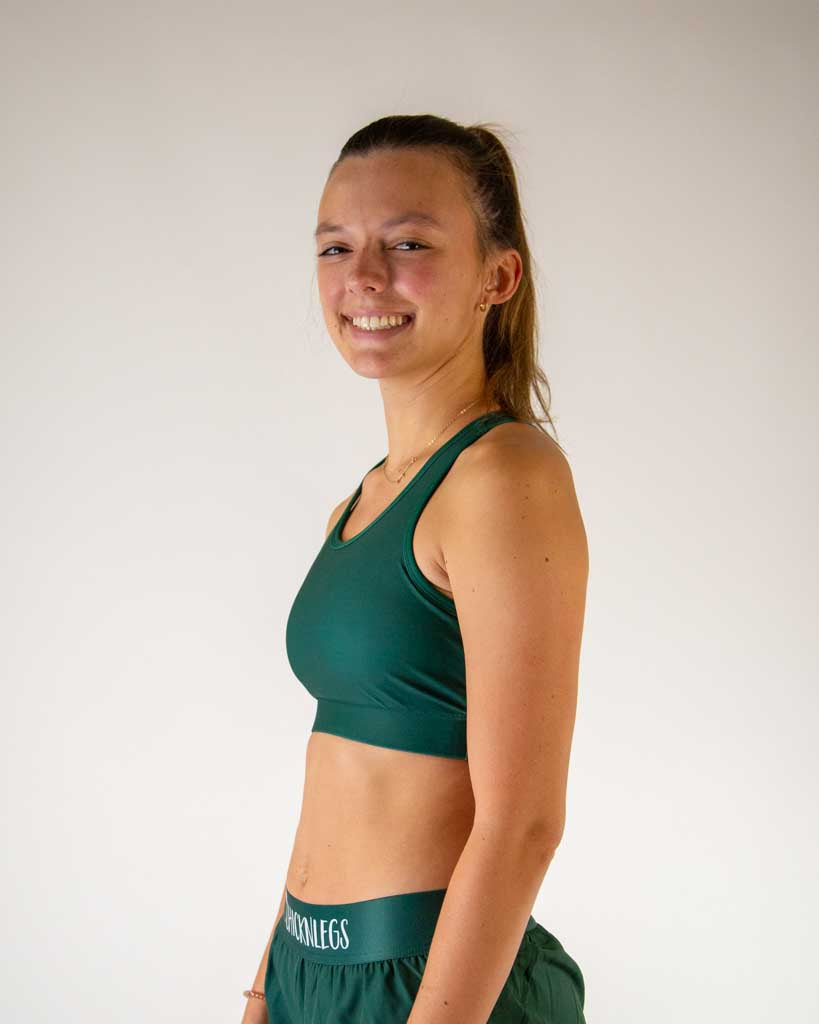 Woman wearing forest green ChicknLegs sports bra and matching shorts, smiling at camera