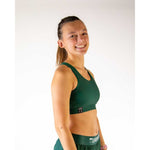 Woman wearing forest green sports bra and matching athletic shorts, smiling