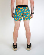 Back view of man wearing teal blue shorts with orange chicken nugget dinosaur pattern