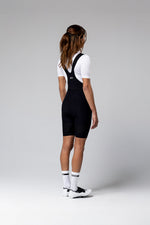 Woman wearing black Gobik Ultralite bib shorts with white shirt, studio shot from behind
