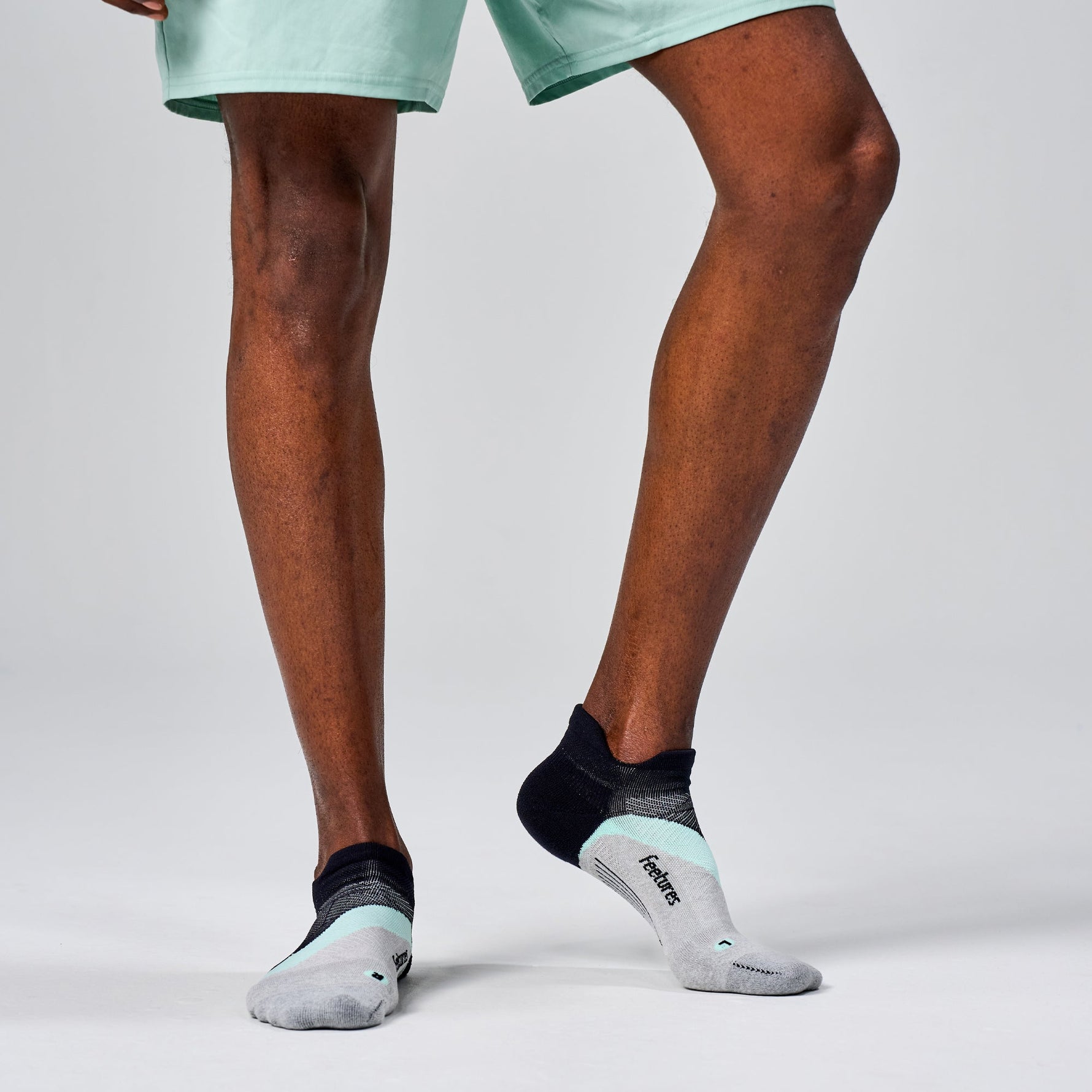 Feetures Elite Light Cushion Tab socks in grey with mint accents on runner's feet