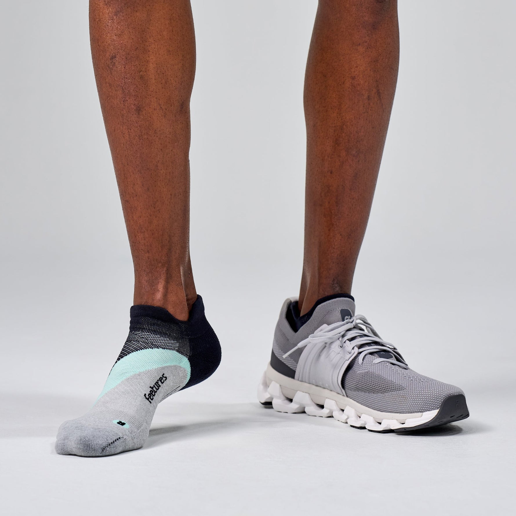 Feetures Elite Light Cushion Tab socks in grey with running shoes on model's feet