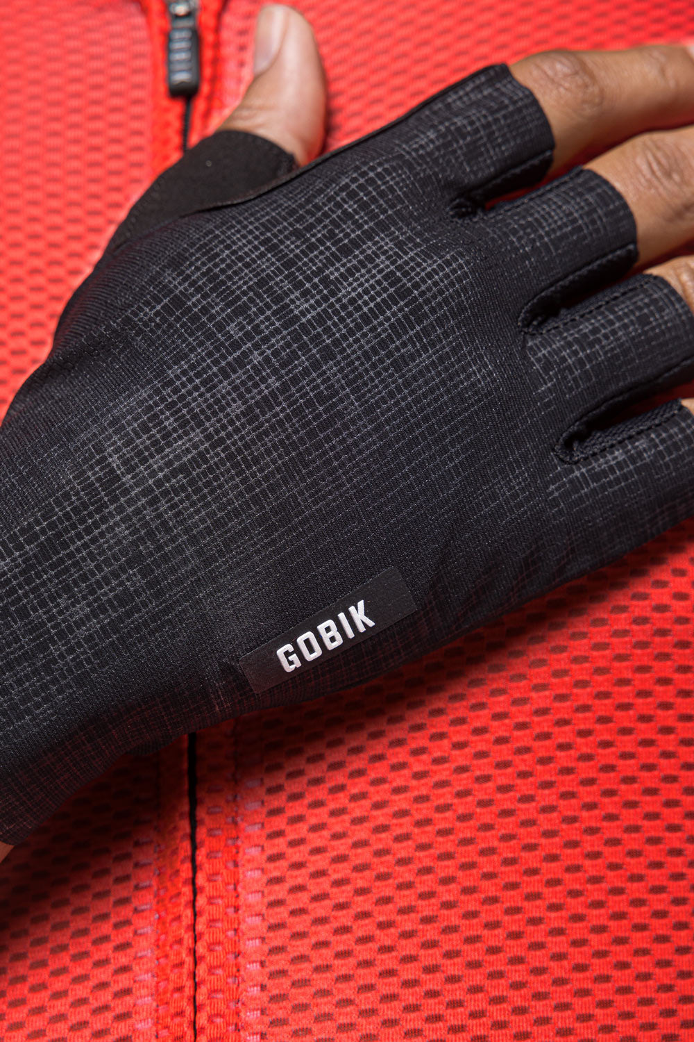 Black Gobik cycling gloves with textured palm grip on red background