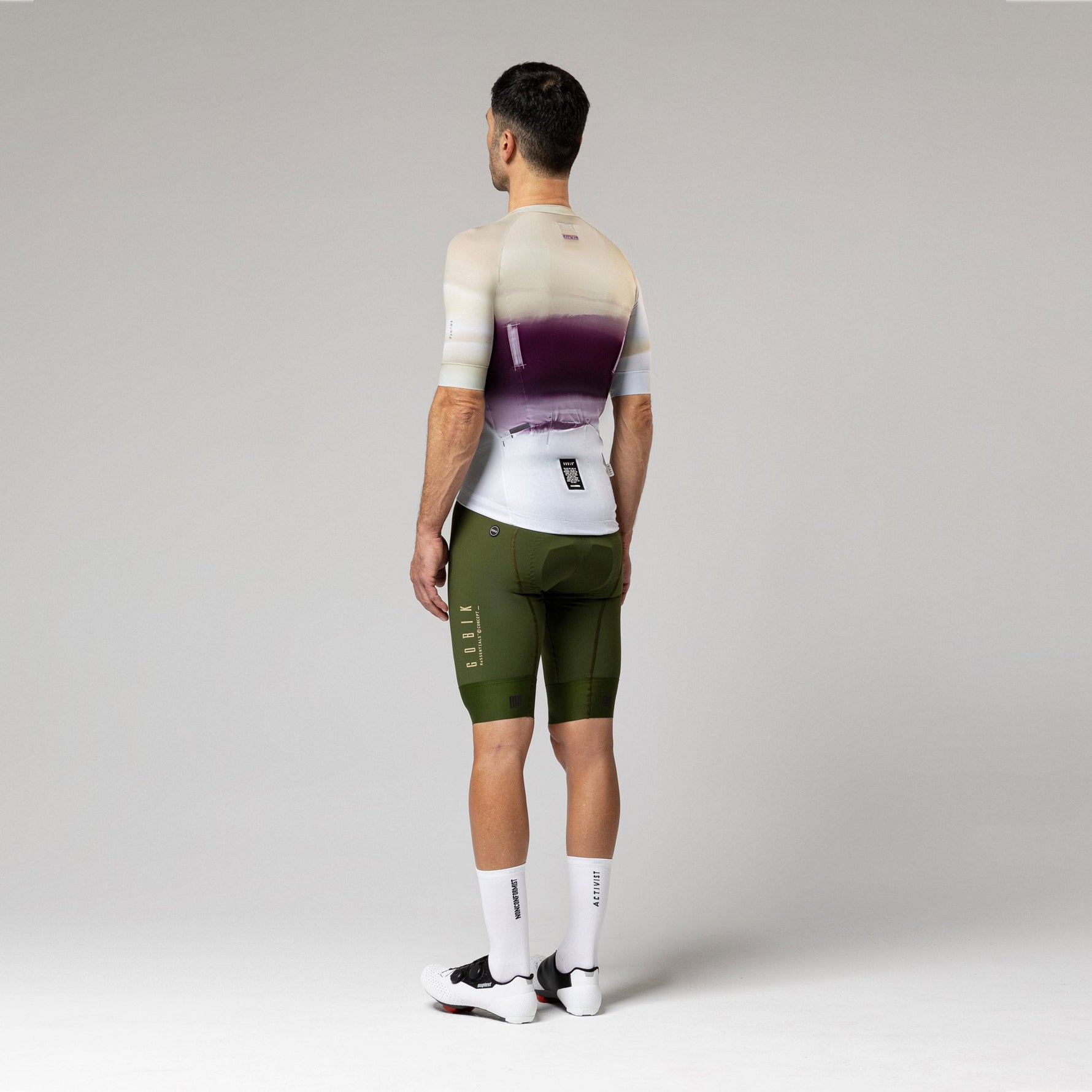 Male cyclist wearing Gobik CX-Pro jersey in Teaberry colorway with olive green bib shorts, rear view