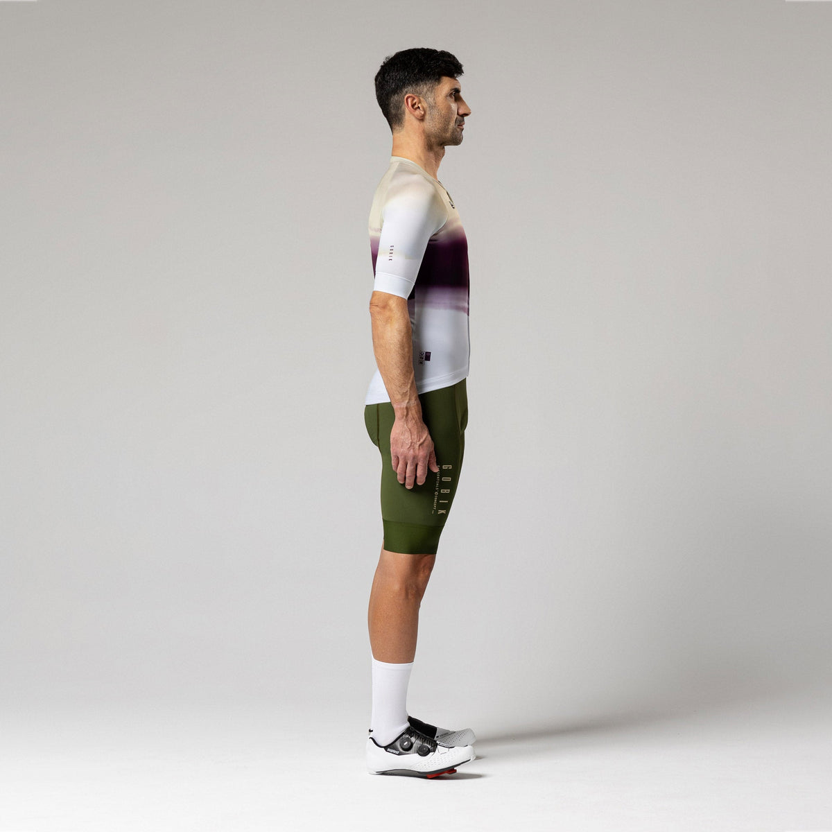 Male cyclist wearing Gobik CX-Pro jersey in Teaberry colorway with olive green bib shorts, side view