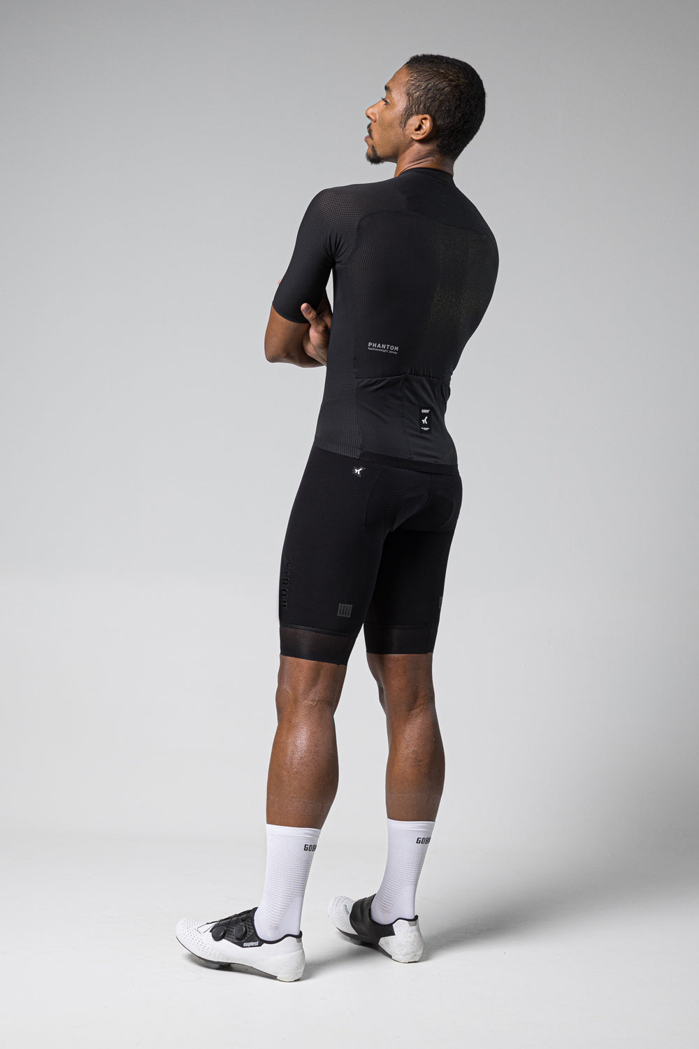 Male cyclist wearing black Gobik Phantom jersey and shorts in studio setting
