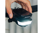 Ravemen FR1100 bike front light mounted under Garmin GPS computer on bicycle handlebars, illuminated