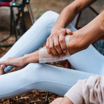 Person applying Ben's insect repellent wipe to lower leg while sitting outdoors at a campsite