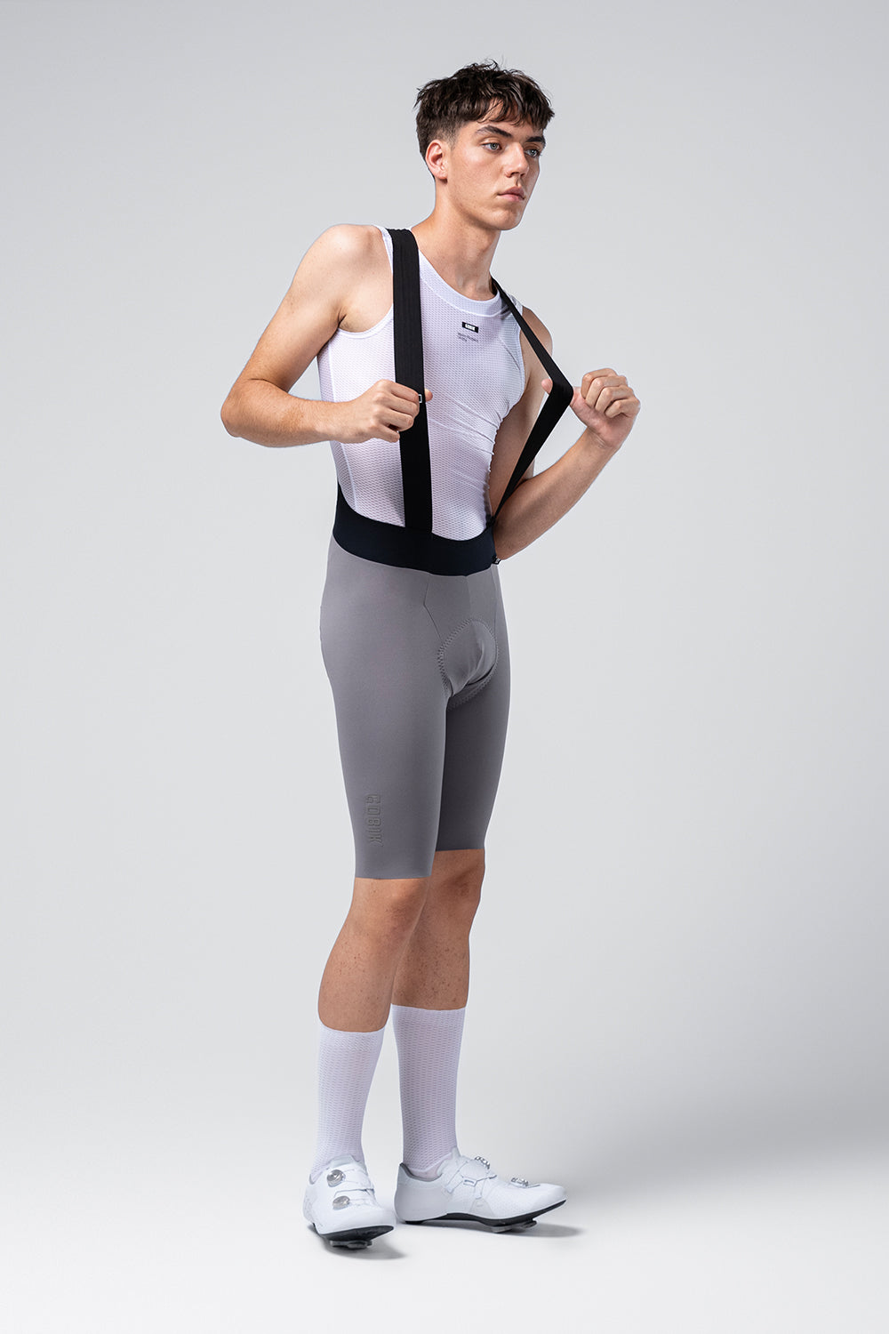 Male cyclist wearing grey Gobik X bib shorts with white tank top and cycling shoes