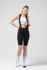 Woman wearing black Gobik X bib shorts with suspenders and white sports bra