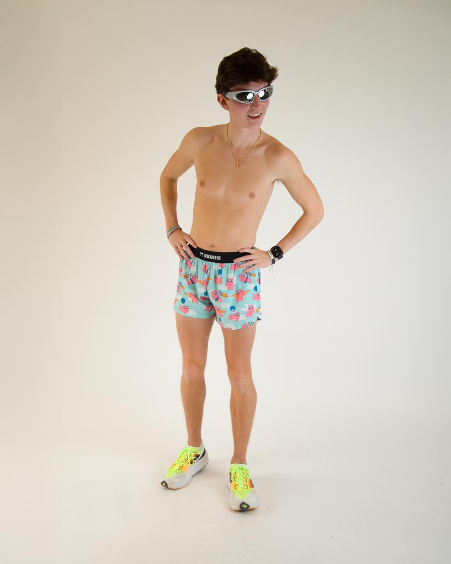 Man wearing ChicknLegs flying pigs print shorts in turquoise with colorful tropical pattern