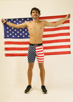 Man wearing ChicknLegs USA flag patterned half tights holding American flag