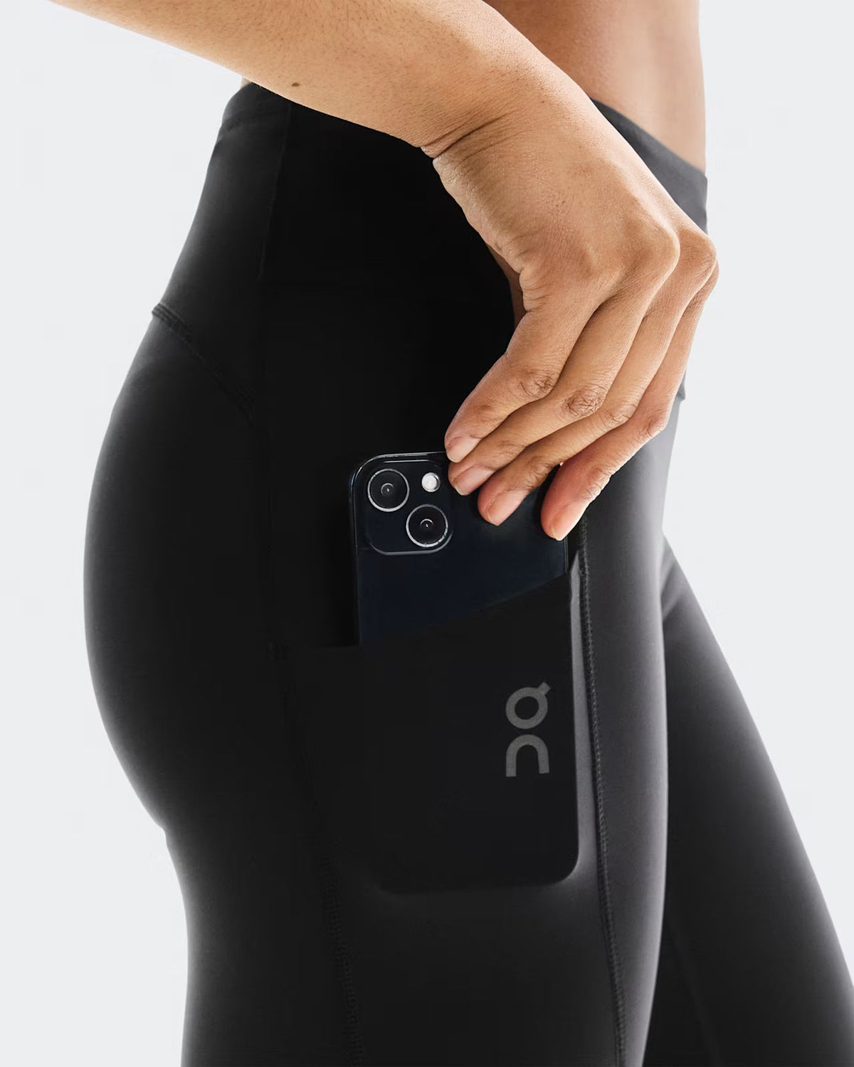 Side view of On Running black tights showing phone being placed into side pocket