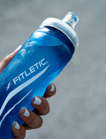 Hand holding wet Fitletic Flow Max Soft Flask 500ml blue bottle showing brand logo clearly.