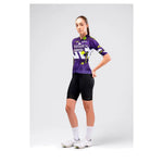 Female cyclist wearing Gobik CX Pro 4.0 violet jersey with black bib shorts and white cycling shoes