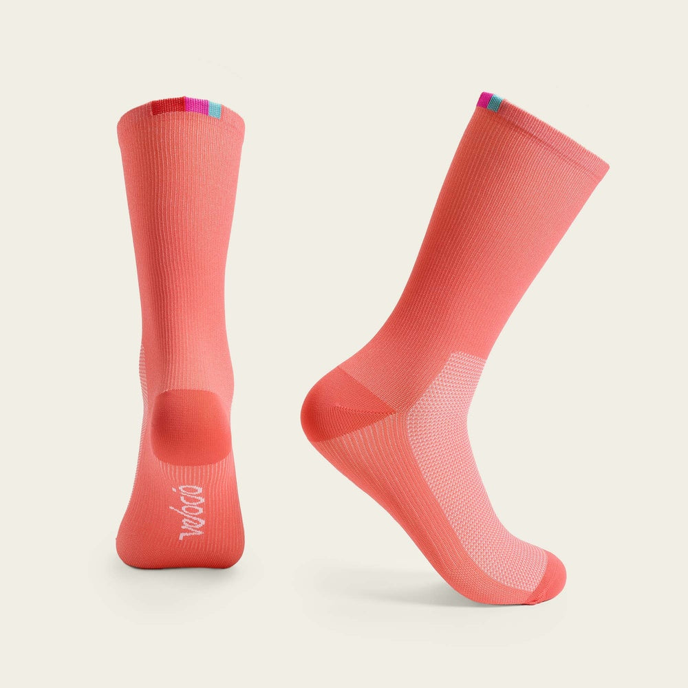Coral pink Velocio cycling socks with colorful heel detail, professional product photography