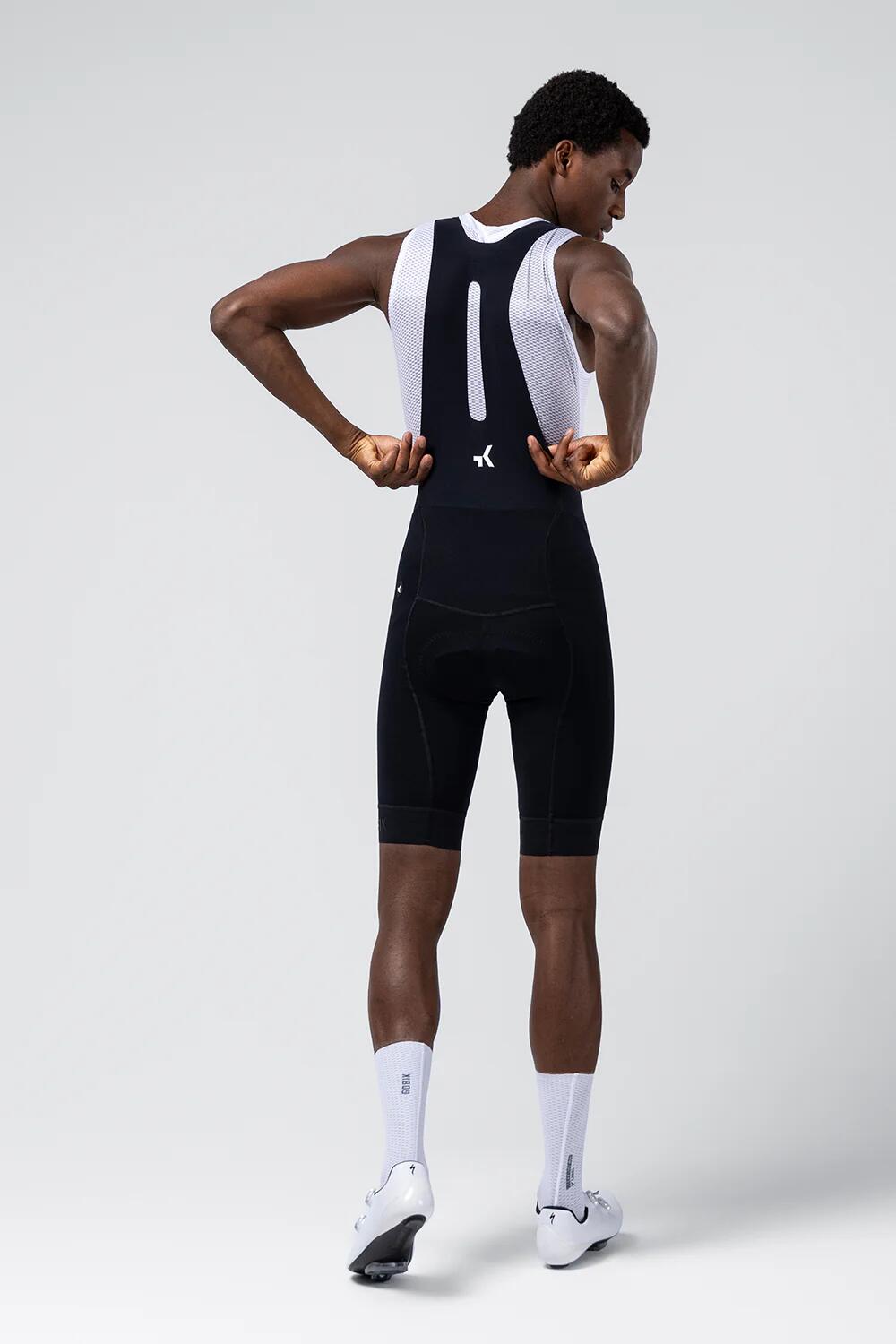 Male cyclist wearing Gobik black bib shorts with white base layer, rear view showing back panel