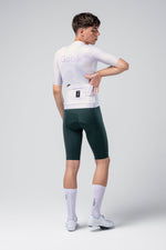 Male cyclist wearing Gobik white jersey and dark green bib shorts, rear view
