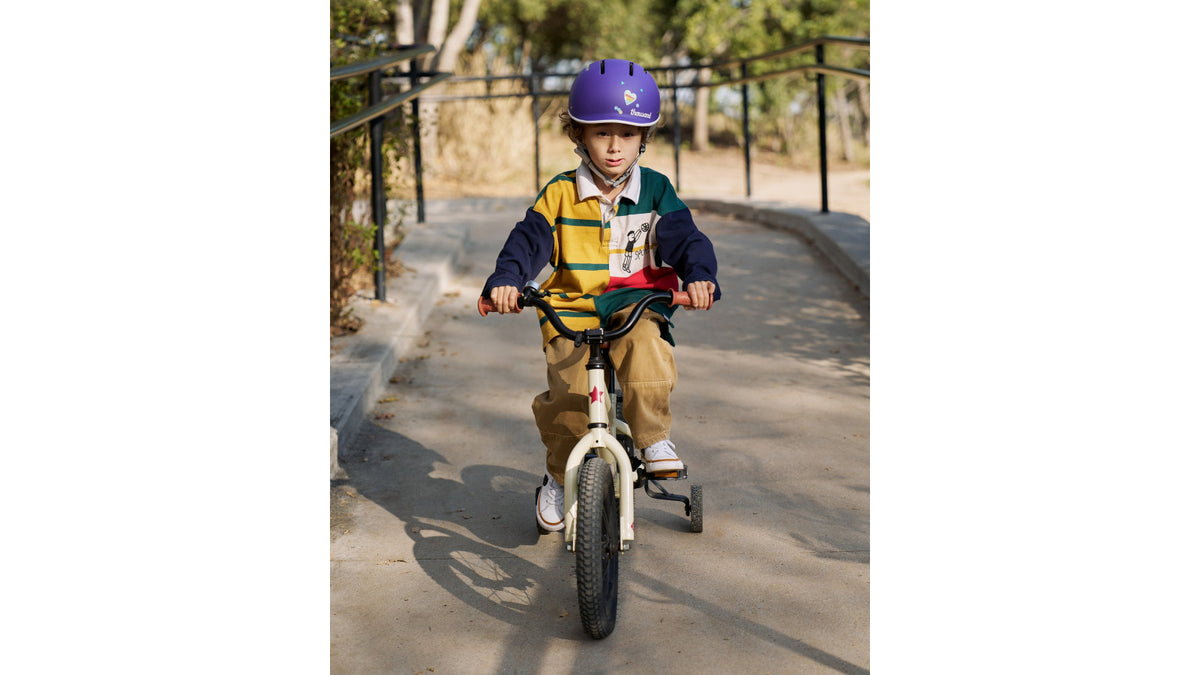 Young child riding a bicycle outdoors wearing the Thousand JR purple kids helmet